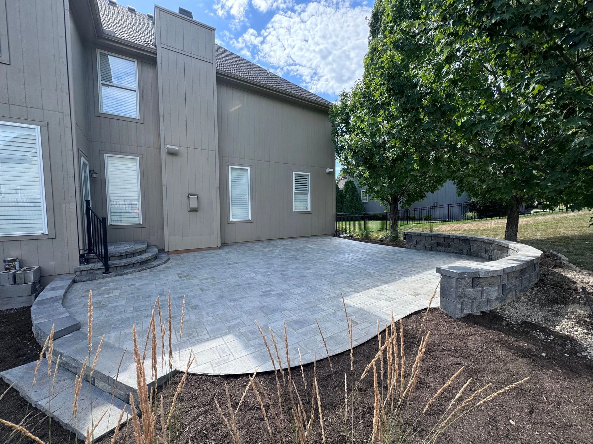 Stamped concrete patio with a seating wall behind a modern home built by Boyt Home Improvement